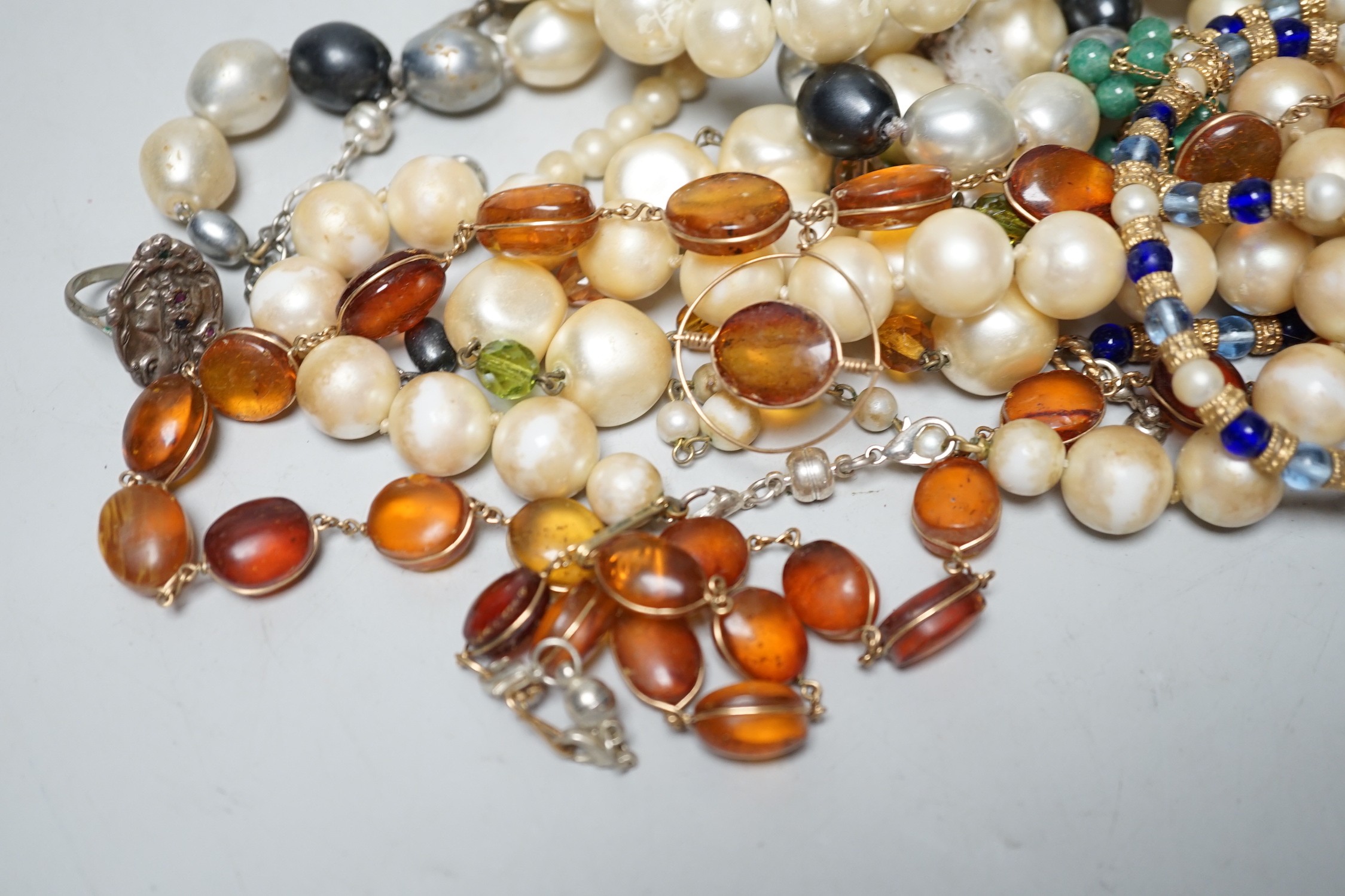 An Art Nouveau style white metal (stamped silver) and gem set ring, a glass bead necklace, an amber necklace and assorted simulated pearl necklaces.